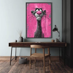 May include: A framed artwork featuring a stylized panther with a pink nose and a pink and gray background. The panther is depicted in black and gray with expressive eyes and long whiskers. The artwork is displayed on a wooden desk.