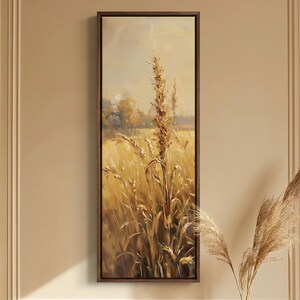 May include: A framed landscape painting depicts a field of wheat in shades of gold and brown. The artwork is displayed on a wall above a wooden table. A vase with dried ornamental grass sits on the table, adding to the rustic theme.
