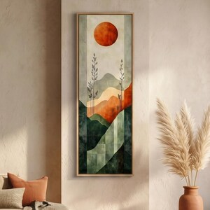 May include: Abstract landscape painting in a vertical rectangular format. The artwork features a large orange sun, stylized mountains in shades of green, orange, and beige, and tall, thin plants. The painting is framed in a light brown wooden frame.