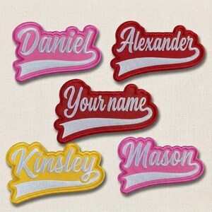 Puede incluir: Cinco parches bordados con nombres en varios colores. Los nombres "Daniel", "Alexander", "Your name", "Kinsley" y "Mason" se muestran en una fuente cursiva con un contorno blanco. Cada parche tiene un diseño de banner.