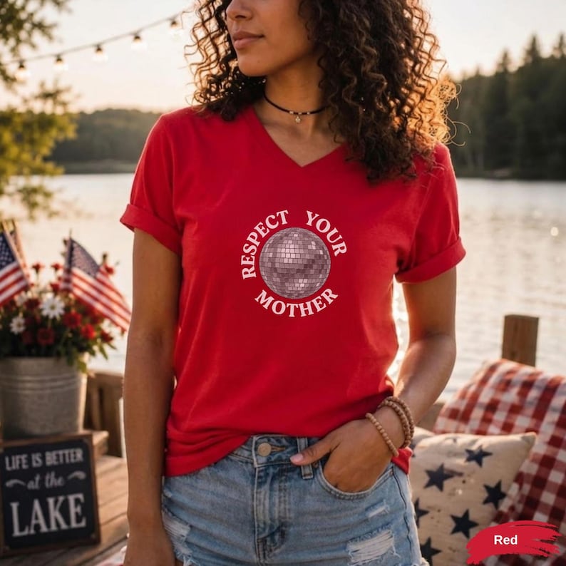 May include: A red V-neck t-shirt featuring a graphic of a silver disco ball in the center, surrounded by the white text "RESPECT YOUR MOTHER" arranged in a circular pattern. The shirt has short sleeves and a standard fit.