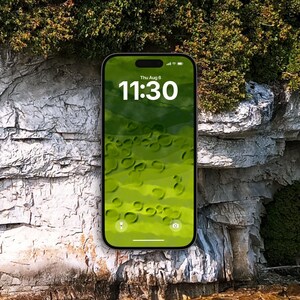 Peut inclure: Un smartphone au cadre noir affichant un écran de verrouillage numérique avec la date Thu Aug 6 et l'heure 11:30 en texte blanc. Le fond d'écran présente un paysage abstrait vert avec des formes circulaires sur un fond de falaise rocheuse.