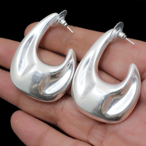 May include: A pair of silver-coloured, teardrop-shaped earrings. The earrings have a smooth, polished surface and a post-and-clutch closure. The design is a modern, minimalist style, suitable for everyday wear or special occasions.