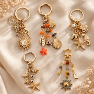 Può includere: Cinque portachiavi in metallo color oro con vari ciondoli tra cui soli, lune, stelle, conchiglie, stelle marine, una tartaruga, un cavalluccio marino e perline colorate. Ogni portachiavi è fissato a un anello circolare con vari ciondoli.