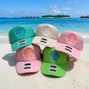 May include: A collection of five foam trucker hats in teal, beige, light pink, bright pink, and lime green. Each hat features a centered embroidered seashell design on the front panel and a rectangular Otto brand label on the brim.