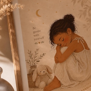 May include: A framed wall art print in warm beige tones featuring an illustration of a person with dark curly hair in a bun, wearing a light dress, sitting with a plush bunny toy. The text reads Be gentle with yourself under a moon and stars.
