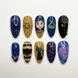 May include: A set of ten almond-shaped press-on nails featuring detailed hand-painted designs including a character with blue hair, a black cat, swirling purple and blue patterns, yellow polka dots, horizontal stripes, and attached button embellishments.