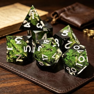 Può includere: Un set di dadi poliedrici realizzati in resina trasparente con fogliame verde simile a muschio incorporato e numeri bianchi in grassetto. La collezione include un d4, d6, d8, d10, d12 e d20, ciascuno con bordi affilati e una finitura trasparente.