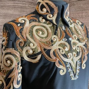 May include: Black equestrian show shirt with elaborate gold, copper, and pearl-like embellishments. The design features swirling patterns and sparkling accents. The word "Signature" is printed on the lower right.