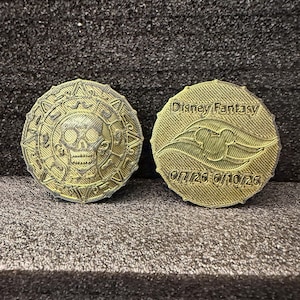 May include: Two gold-colored coins. One coin features a skull and crossbones design, while the other has the words "Disney Fantasy" and a ship illustration. The date "6/7/26 - 6/10/26" is also visible.