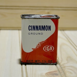 May include: A vintage red and white metal tin with the text "CINNAMON GROUND" and the IGA logo. The tin has a net weight of 1 1/4 oz.