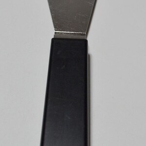 Pode incluir: Uma esp&aacute;tula de a&ccedil;o inoxid&aacute;vel com cabo preto. A esp&aacute;tula tem uma l&acirc;mina larga e plana e um cabo arredondado. A l&acirc;mina tem aproximadamente 7,6 cm de largura e 10,2 cm de comprimento. O cabo tem cerca de 10,2 cm de comprimento.
