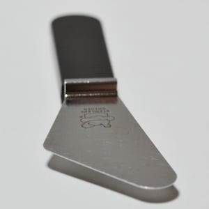 Pode incluir: Uma faca de queijo em a&ccedil;o inoxid&aacute;vel com cabo escuro e l&acirc;mina triangular. A l&acirc;mina tem um design gravado e o texto "STAINLESS SWEDEN". A faca foi projetada para cortar queijo.