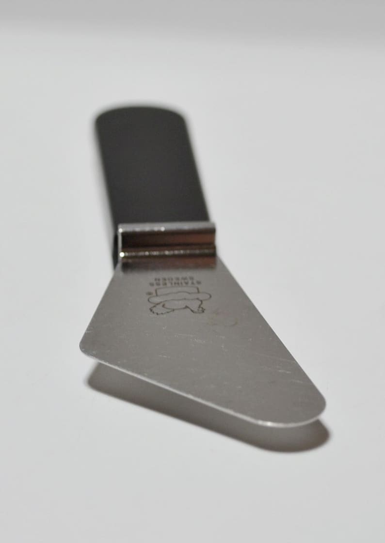 Pode incluir: Uma faca de queijo em a&ccedil;o inoxid&aacute;vel com cabo escuro e l&acirc;mina triangular. A l&acirc;mina tem um design gravado e o texto "STAINLESS SWEDEN". A faca foi projetada para cortar queijo.