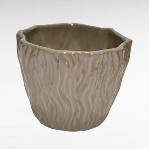 May include: A brown ceramic planter with a textured bark-like design. The planter is a simple, round shape with a wide opening.