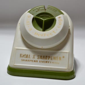 May include: A white and green Dial X Sharpener. The knife sharpener has a green base and a white body with a green top. The text "Dial a perfect edge" is printed on the top. The text "Sharpens Everything" is printed on the front.