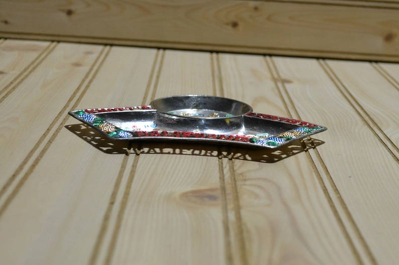 Puede incluir: Una bandeja de plata con un borde decorativo de cuentas rojas, verdes y doradas. La bandeja tiene una peque&ntilde;a depresi&oacute;n redonda en el centro.