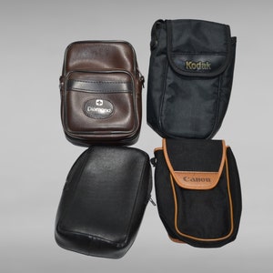 May include: Four camera cases in different colors and styles. The cases are made of leather and fabric. The cases have the brand names "Kodak", "Canon", and "Diamond" printed on them.