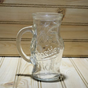 May include: A clear glass mug with a handle. The mug has the words " Frosties Root Beer" embossed on the side.