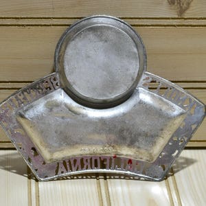 Puede incluir: Un plato de metal plateado con un centro redondo elevado y un borde festoneado. El plato tiene las palabras "California Souvenir" alrededor del borde.