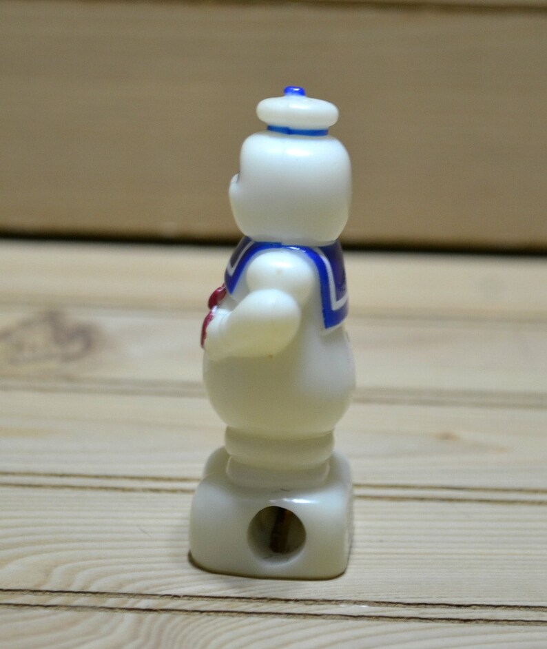 Puede incluir: Sacapuntas de pl&aacute;stico blanco con forma del personaje de los Cazafantasmas, el Stay Puft Marshmallow Man. El sacapuntas tiene un gorro de marinero azul y blanco y una corbata de lazo roja.