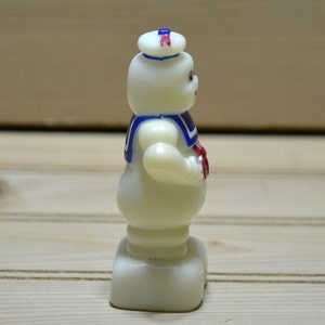 Puede incluir: Una figurita de pl&aacute;stico blanco de un fantasma con un sombrero de marinero azul y rojo y una camisa de marinero azul y blanca. El fantasma est&aacute; de pie sobre una base blanca.