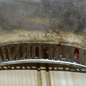 Puede incluir: Una placa de matr&iacute;cula de California de metal plateado con el texto "MADE IN JAPAN" en la parte superior. La placa tiene un dise&ntilde;o recortado de la palabra "CALIFORNIA".