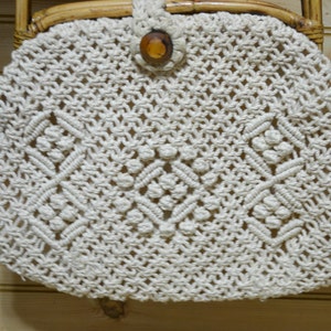 May include: A white crocheted bag with a wooden button closure. The bag has a diamond pattern and is made of thick rope.