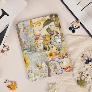 May include: A colorful tablet case featuring Winnie the Pooh and friends. The case has a whimsical design with illustrations of Pooh, Piglet, and other characters, with the word "Honey" in a script font. The background includes flowers and trees.