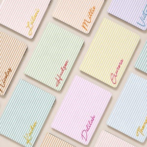 May include: A collection of rectangular notebooks featuring vertical pinstripes in various pastel colors including pink, orange, yellow, green, and blue. Each notebook is personalized with a name written in a cursive script font across the cover.