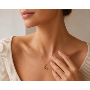 May include: A gold-toned necklace featuring a delicate chain and a pendant shaped like a crescent moon and a sun. The sun element is accented with a small, vibrant red gemstone at its center, creating a celestial-inspired jewelry piece.