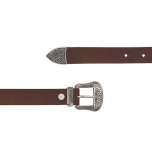 Könnte beinhalten: Ein brauner Ledergürtel mit einer silberfarbenen Schnalle und Spitze. Die Schnalle und die Spitze haben ein verziertes, graviertes Design. Der Gürtel wird vor einem weißen Hintergrund gezeigt.