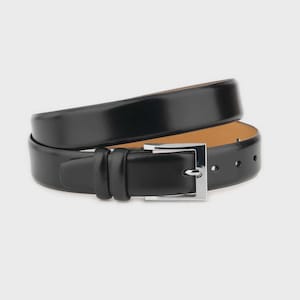Peut inclure: Une ceinture en cuir noir enroulée, avec une boucle carrée argentée. La surface lisse et brillante de la ceinture est mise en évidence, ainsi que l'intérieur de couleur plus claire. Design classique et minimaliste.