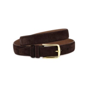 Könnte beinhalten: Ein dunkelbrauner Wildleder-Gürtel mit einer goldfarbenen Schnalle. Der Gürtel ist aufgerollt und zeigt die Textur des Wildleders und den Glanz der Schnalle. Ein klassisches Accessoire.
