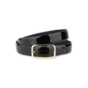 Pode incluir: Um cinto de couro envernizado preto com uma fivela retangular dourada. O cinto está enrolado, mostrando seu acabamento brilhante. A fivela tem um design simples e elegante, complementando o visual elegante do cinto.