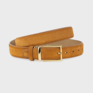 Peut inclure: Une ceinture en daim de couleur beige avec une boucle rectangulaire dorée. La ceinture est d'une teinte chaude et terreuse et présente un design classique. La ceinture est probablement en cuir suédé véritable.