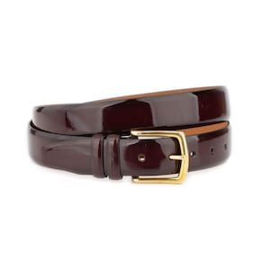 May include: A rolled-up, burgundy leather belt with a glossy finish and a gold-coloured buckle. The buckle is rectangular with rounded corners. The belt is designed for trousers.