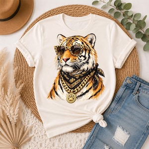 Könnte beinhalten: Ein cremefarbenes Kurzarm-T-Shirt mit einem Grafikdruck eines Tigers, der eine Sonnenbrille mit Leopardenmuster, ein schwarz gemustertes Bandana und eine dicke goldene Kette mit einem runden Anhänger mit Pfotenabdruck trägt.