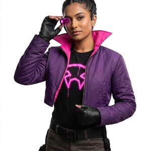 May include: A cropped purple jacket with a bright pink interior lining and collar, worn over a black t-shirt featuring a neon pink graphic design. The outfit includes black fingerless gloves, a black belt, and dark gray pants with utility pouches.