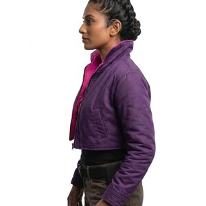 May include: A cropped jacket in a deep purple hue featuring a high collar and a vibrant hot pink interior lining. The jacket has long sleeves, a front zipper closure, and two side pockets, worn over a black top and dark brown utility trousers.