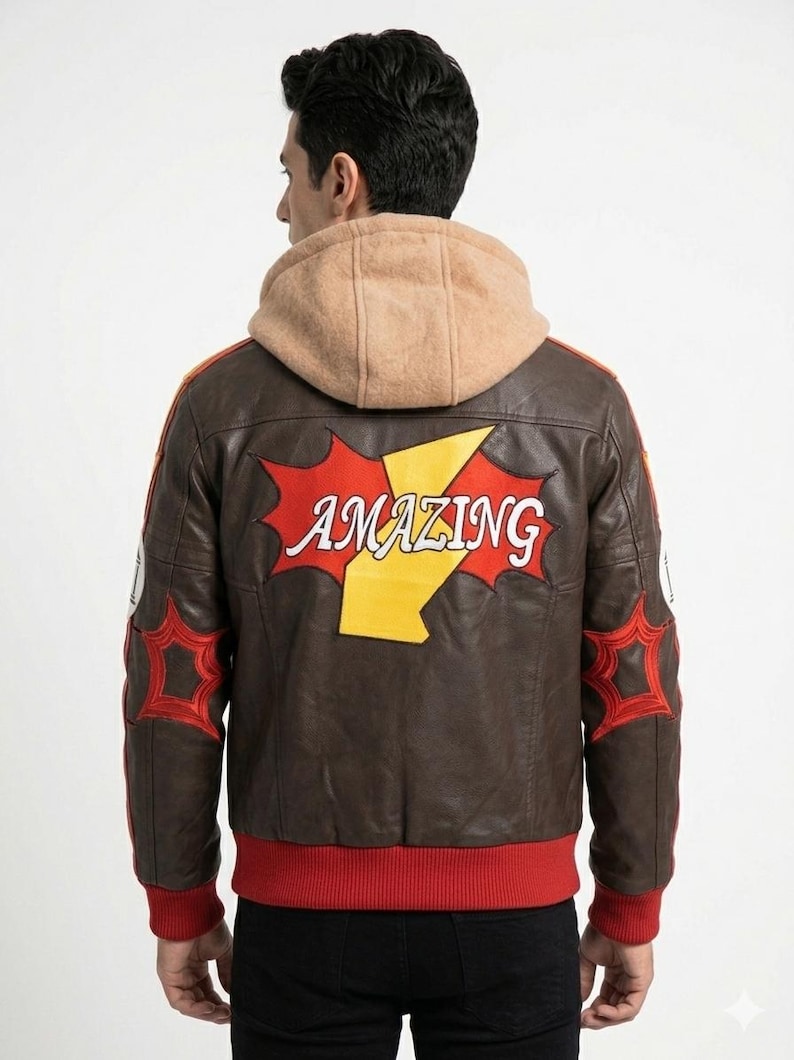 K&ouml;nnte beinhalten: Eine braune Lederjacke mit beigefarbener Kapuze, rotem Rippsaum und roten Rippb&uuml;ndchen. Auf der R&uuml;ckseite befindet sich ein gro&szlig;es rot-gelbes Grafik-Patch mit dem Wort AMAZING in wei&szlig;er Schrift sowie rote sternf&ouml;rmige Aufn&auml;her an den &Auml;rmeln.