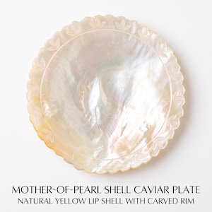 Puede incluir: Un plato circular para caviar hecho de nácar de concha de labio amarillo natural. El cuenco presenta una superficie iridiscente y nacarada, con un borde festoneado que muestra un delicado patrón tallado en forma de hojas alrededor de todo el perímetro.