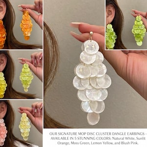 May include: Dangle earrings featuring a cluster of circular mother-of-pearl discs arranged in a tiered, elongated shape. Available in five colors: natural white, sunlit orange, moss green, lemon yellow, and blush pink. Text reads: OUR SIGNATURE MOP DISC CLUSTER DANGLE EARRINGS - AVAILABLE IN 5 STUNNING COLORS: Natural White, Sunlit Orange, Moss Green, Lemon Yellow, and Blush Pink.