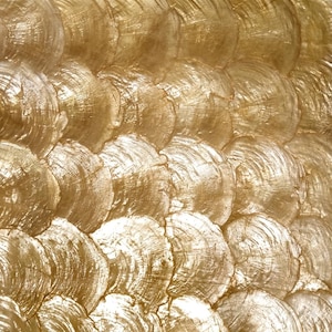 Puede incluir: Un panel decorativo de pared con un patrón repetitivo de elementos circulares dorados superpuestos. Cada pieza circular individual muestra una textura radial en forma de abanico, creando un efecto de superficie metálica brillante.