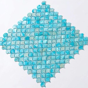 May include: A diamond-shaped mosaic tile sheet featuring a repeating pattern of small, light blue, fan-shaped pieces. Each individual tile has a smooth, iridescent finish that reflects light, creating a layered, scale-like appearance across the surface.