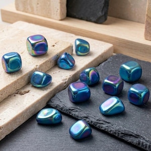 Può includere: Una collezione di piccoli cubi lisci e iridescenti con una finitura metallica che varia tra tonalità di blu, viola e verde. Questi oggetti lucidi e sfaccettati sono sparsi, mostrando una consistenza superficiale riflettente e brillante.