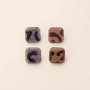May include: Four square-shaped earrings with a textured, animal print design. Two earrings are gray with black markings, and two are brown with dark brown markings. Each earring is framed with a gold-colored, beaded edge.