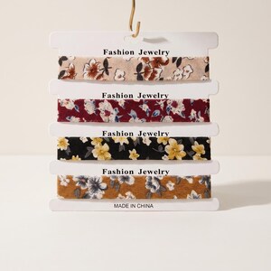 May include: Five floral chokers on display, each on a white card. The chokers have diverse floral patterns in beige, burgundy, black, and mustard yellow. Each card is labelled "Fashion Jewelry".