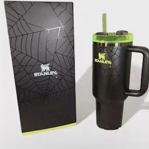 Pode incluir: Caneca Stanley preta com tampa e canudo verdes e caixa a condizer. Tanto a caneca como a caixa apresentam um design de teia de aranha e o log&oacute;tipo Stanley. A caneca tem uma pega e foi concebida para bebidas frias.