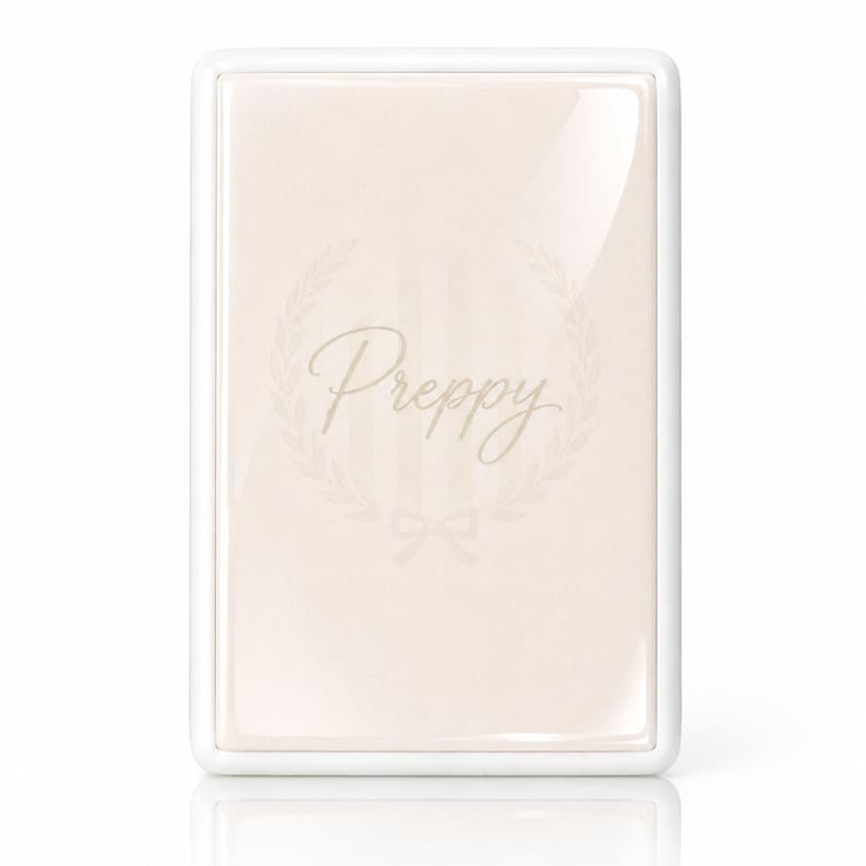 May include: A rectangular, glossy, light beige plaque with a white border. The center features the word Preppy in a cursive script, surrounded by a faint laurel wreath design and a small bow at the bottom, all in a subtle, light-colored tone.